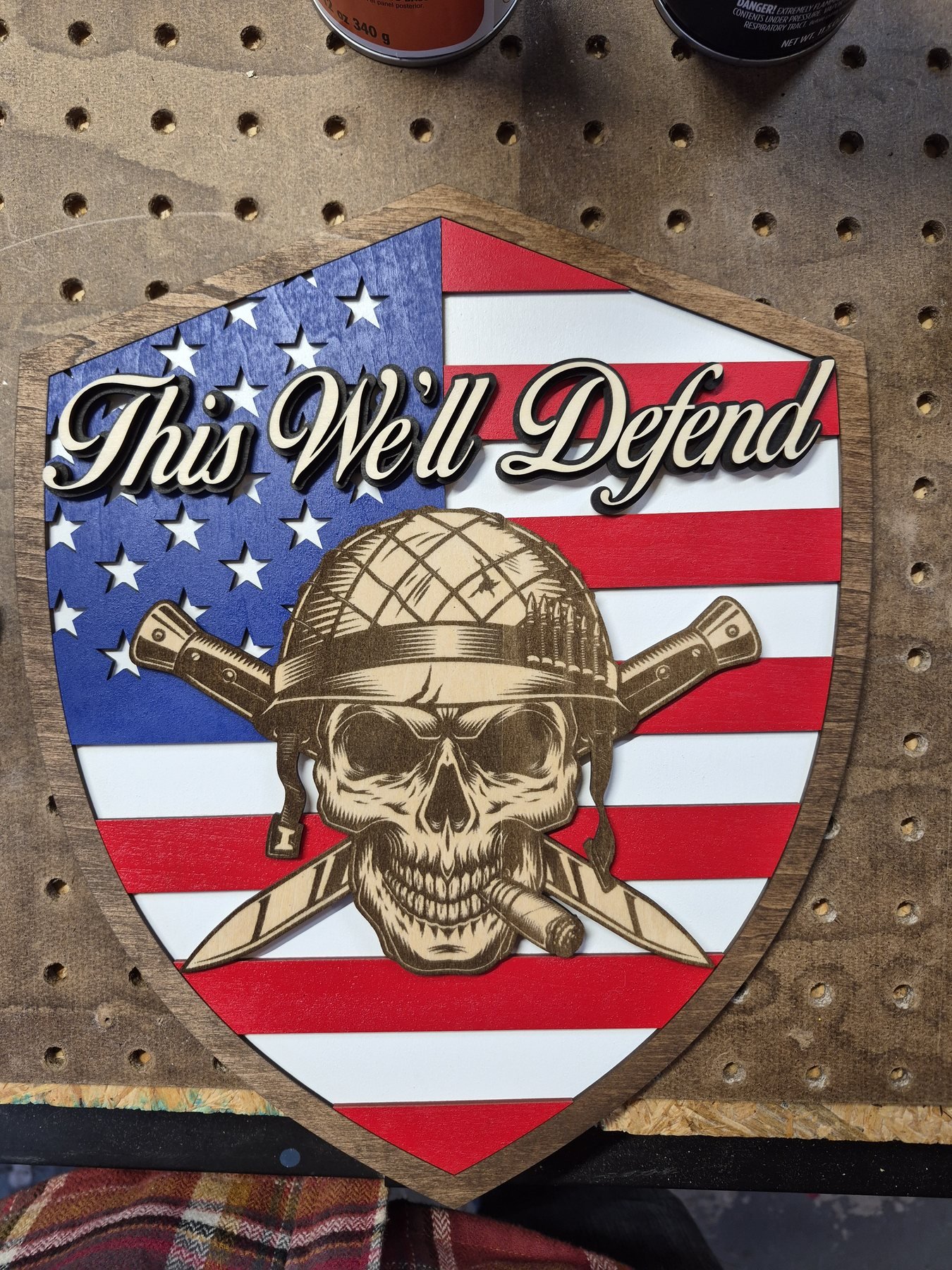 Shield shaped American flag plaque with raised script lettering and an engraved helmeted skull.