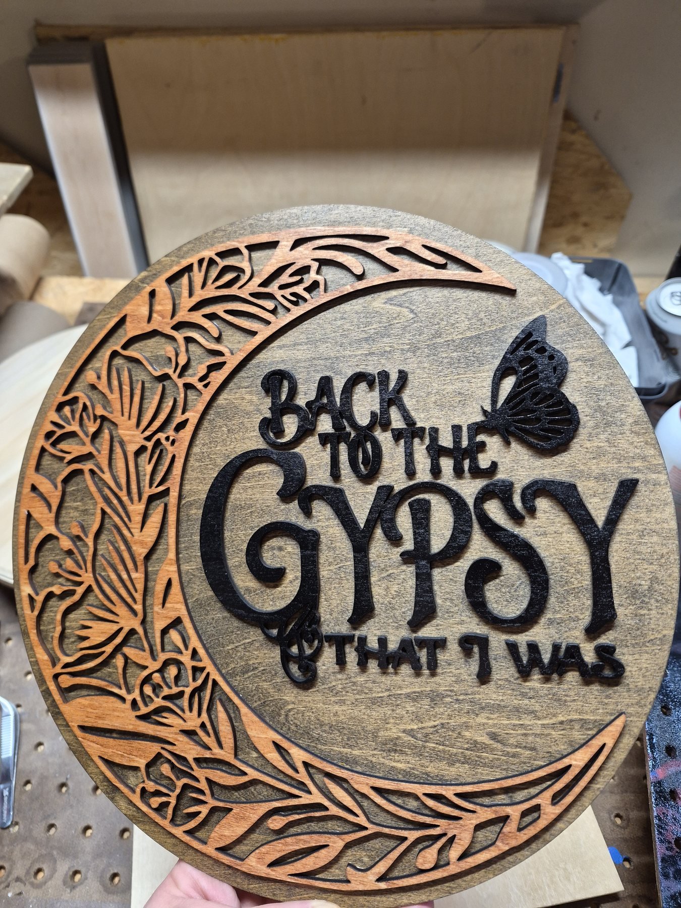 Round wooden moon wall art with layered floral cutouts, a butterfly and decorative lettering.