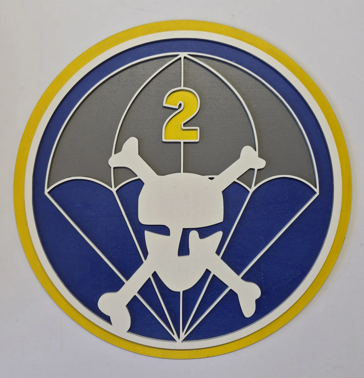 Round parachute unit shield with a winged skull, a number two and blue and gray panels.