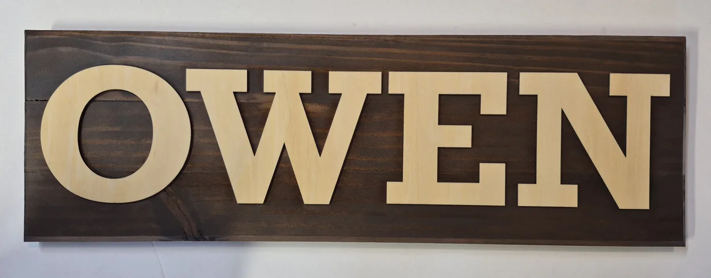 Owen name sign with bold light wood letters on a dark rectangular background.