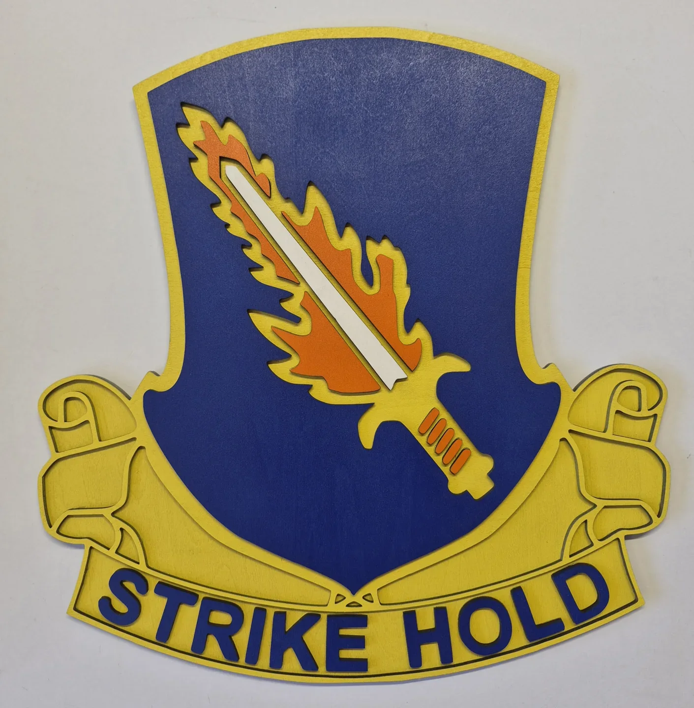 Blue and gold Strike Hold unit crest with a yellow lightning motif and curved scroll.