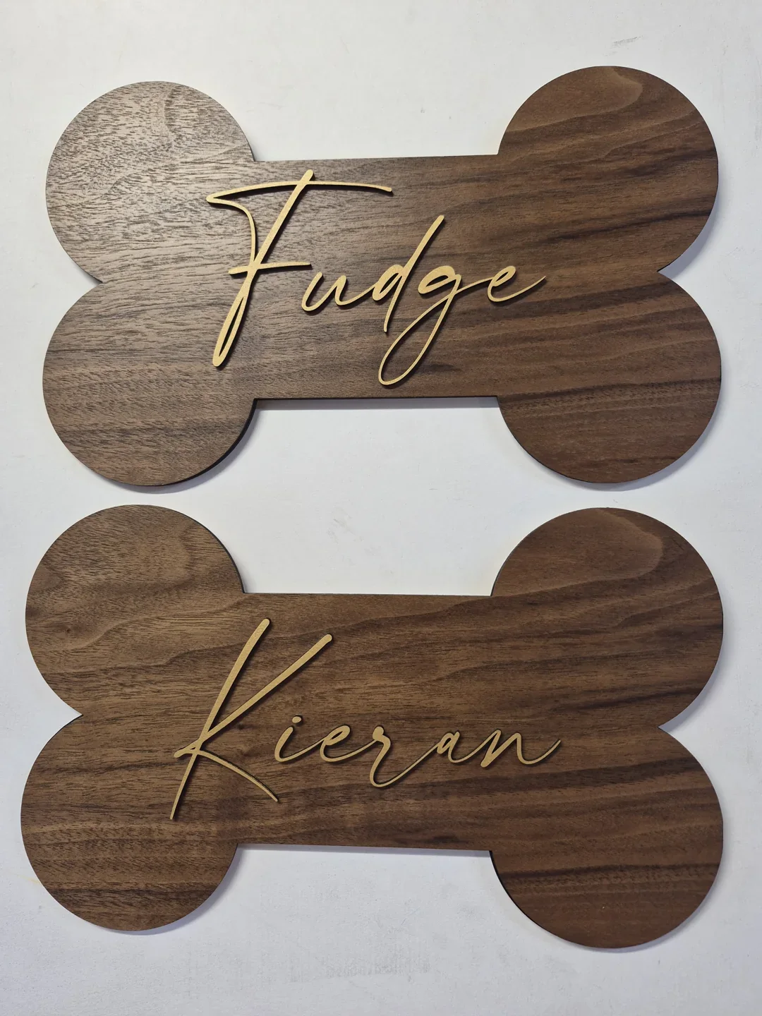 Personalized wooden pet name signs shaped like bones with contrasting wood tones.