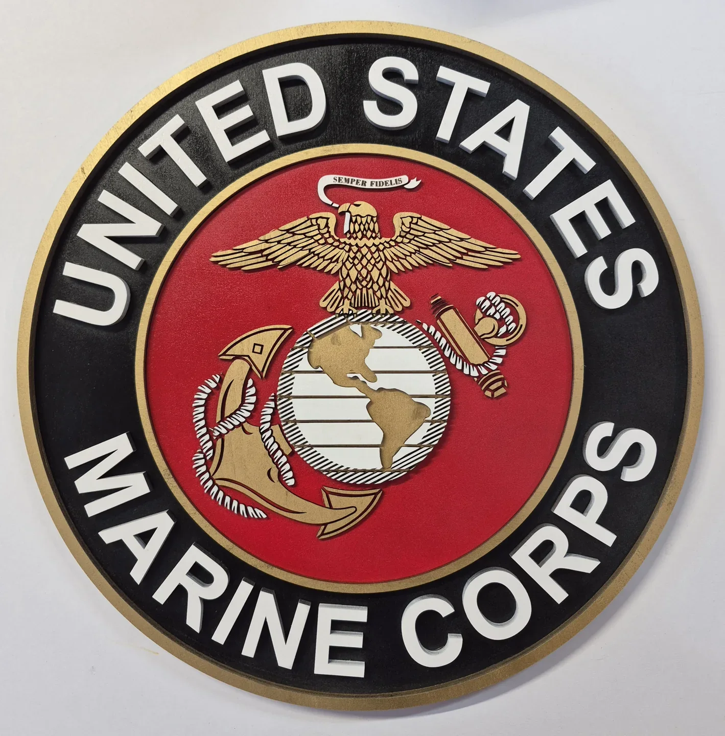 Round United States Marine Corps emblem with a red center and layered gold details.