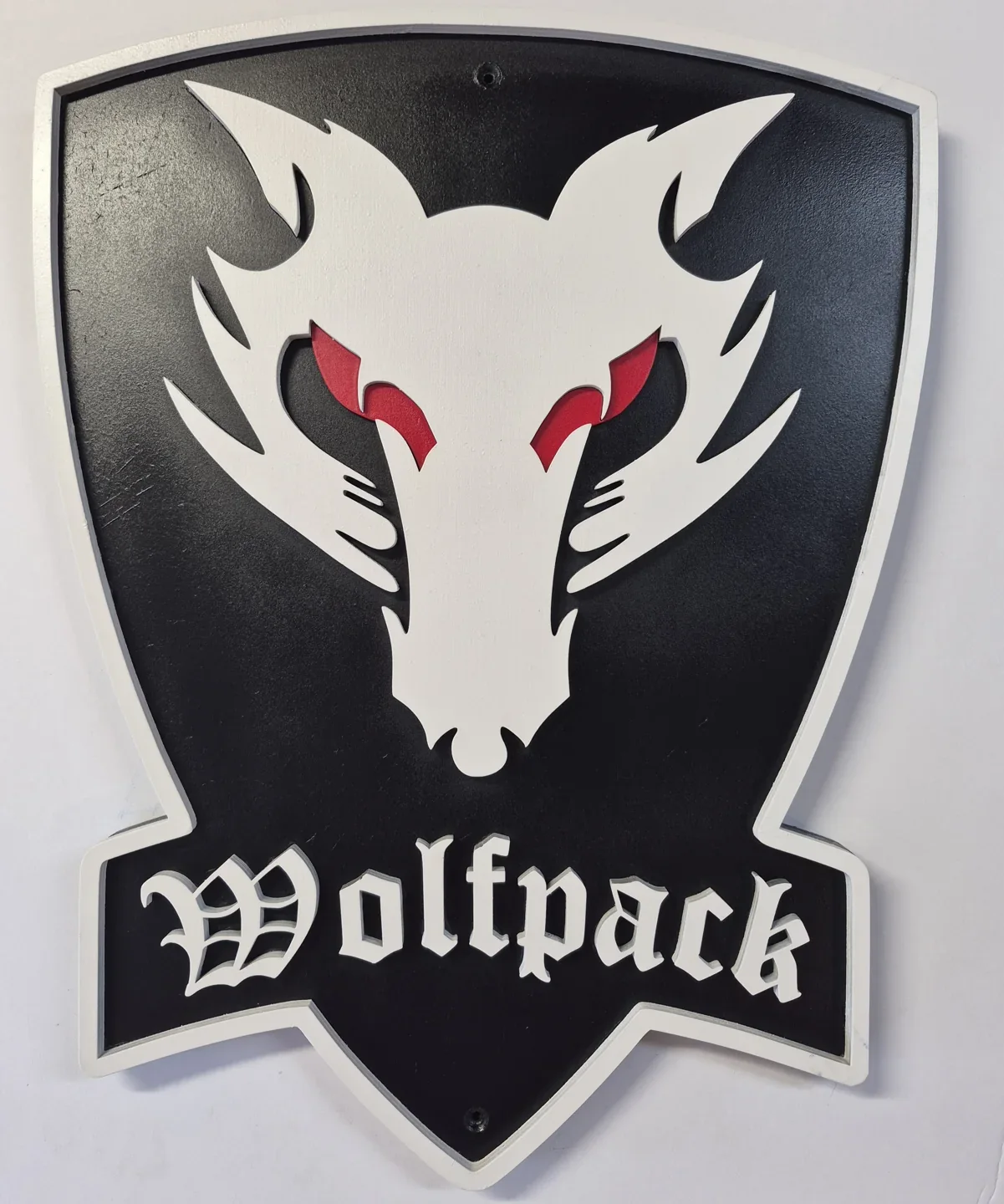 Black Wolfpack shield with a white wolf head, red eyes and raised lettering.