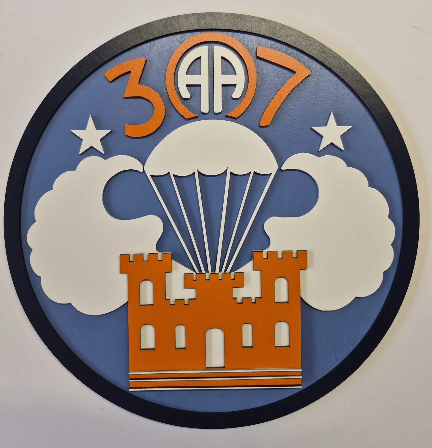 Round Airborne engineer plaque with a parachute, clouds and an orange castle.