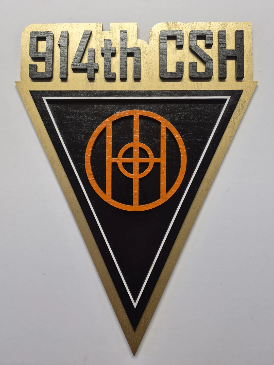 914th CSH triangular shield with gold lettering and a circular central emblem.