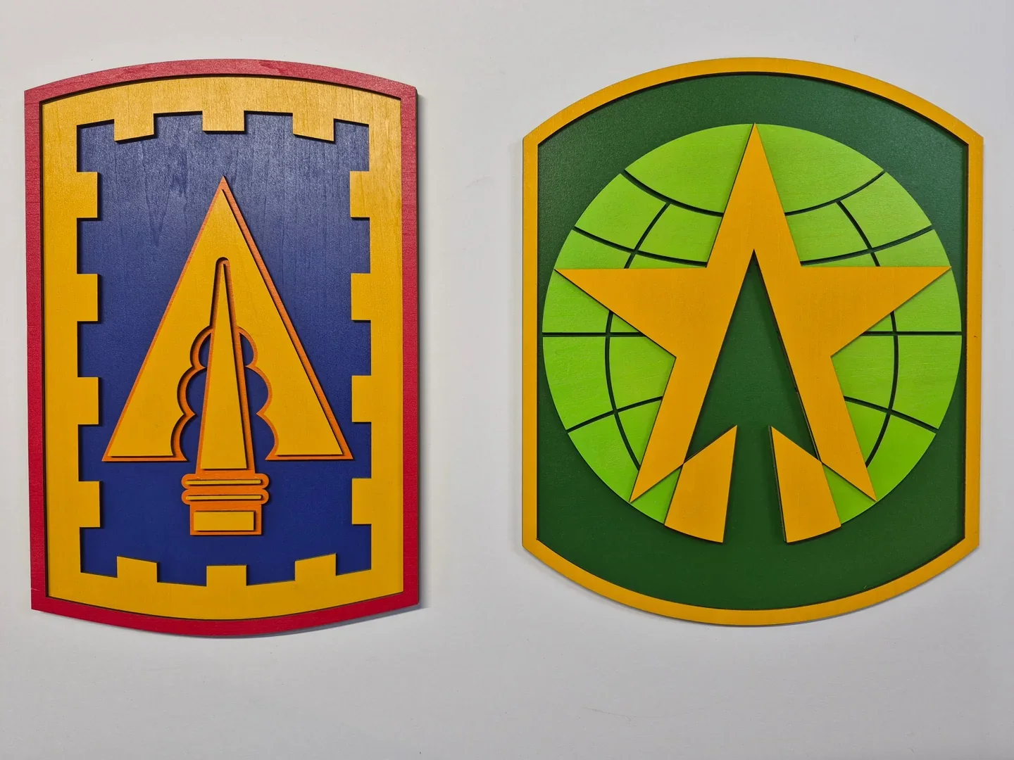 Pair of military shield plaques with colorful layered symbols and contrasting borders.
