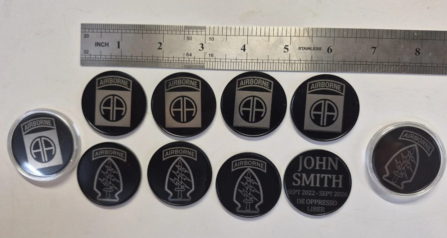 Collection of black metal challenge coins engraved with unit emblems and personalized text.