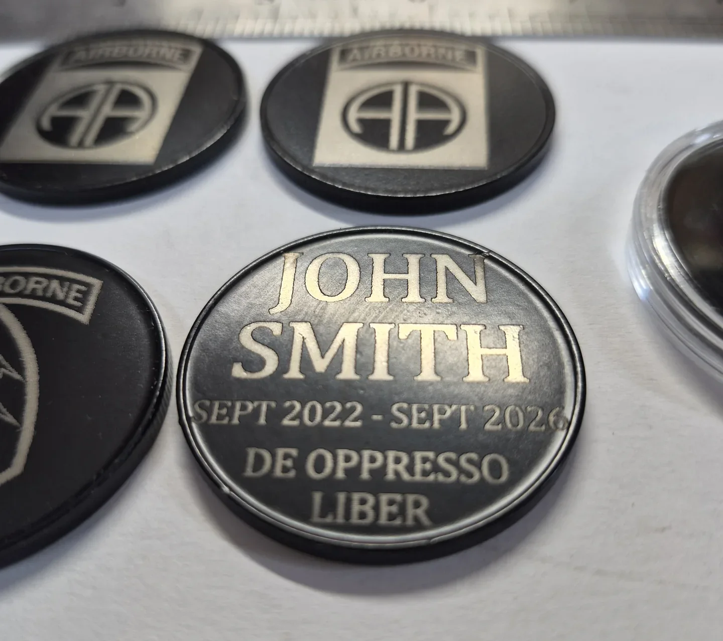 Close view of a personalized black metal challenge coin with engraved presentation lettering.